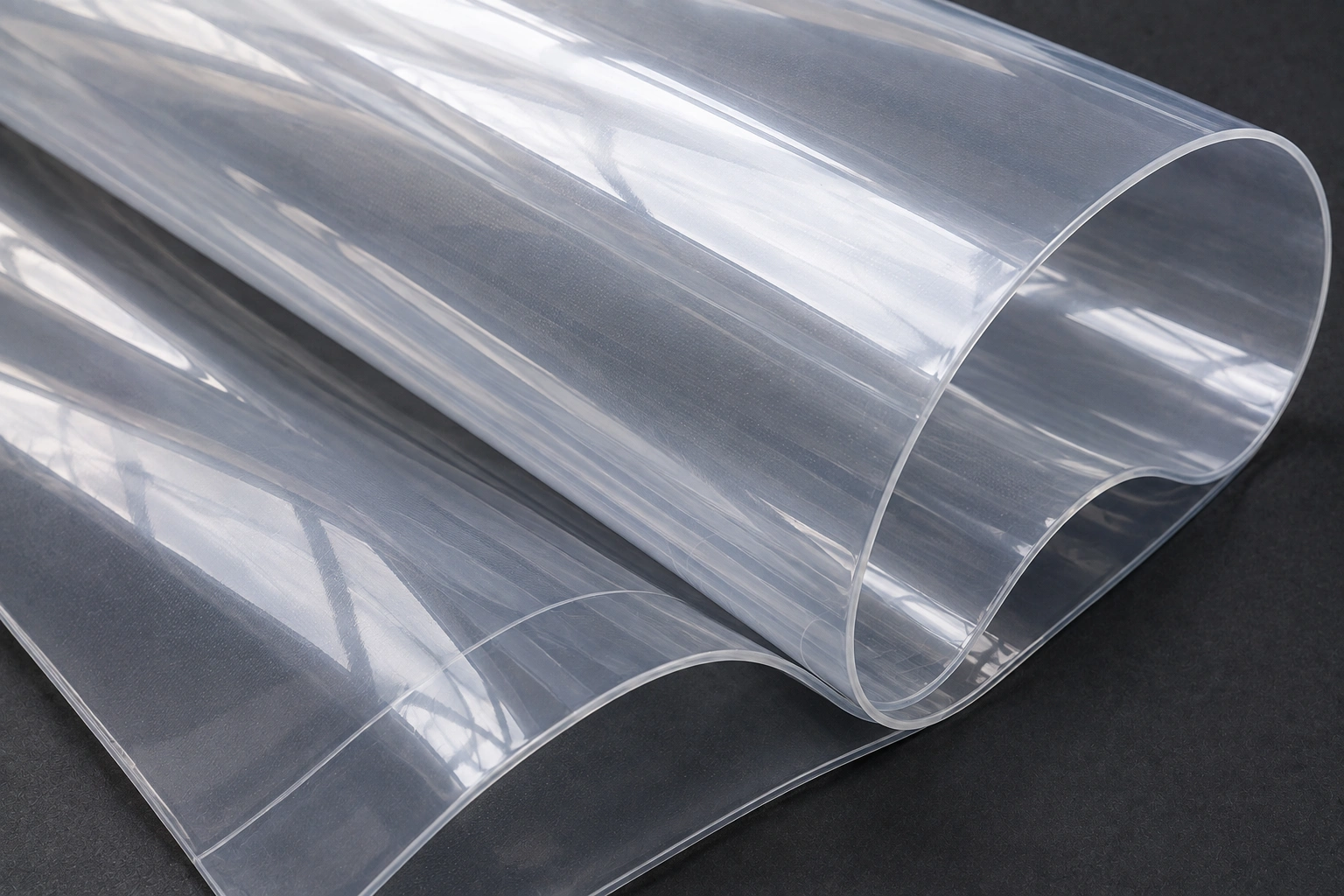 Layers of thin, highly transparent ETFE film curled on a dark surface, showing that it is a clear extruded film and not a woven fabric